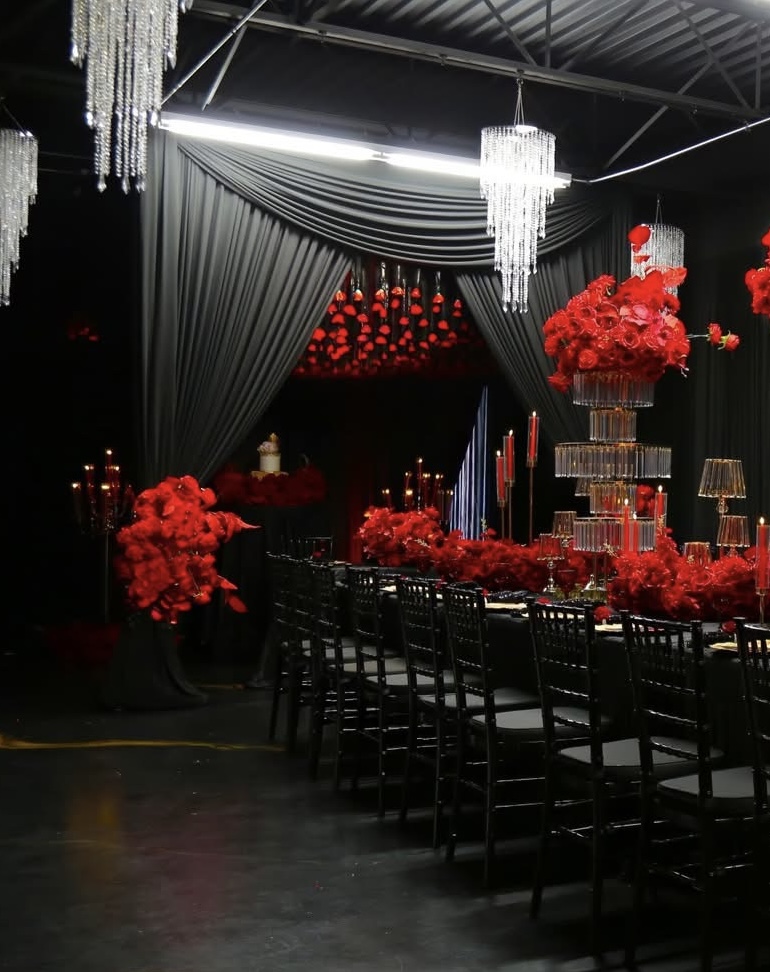 High-drama event space with black draping, red roses, crystal chandeliers and candlelight