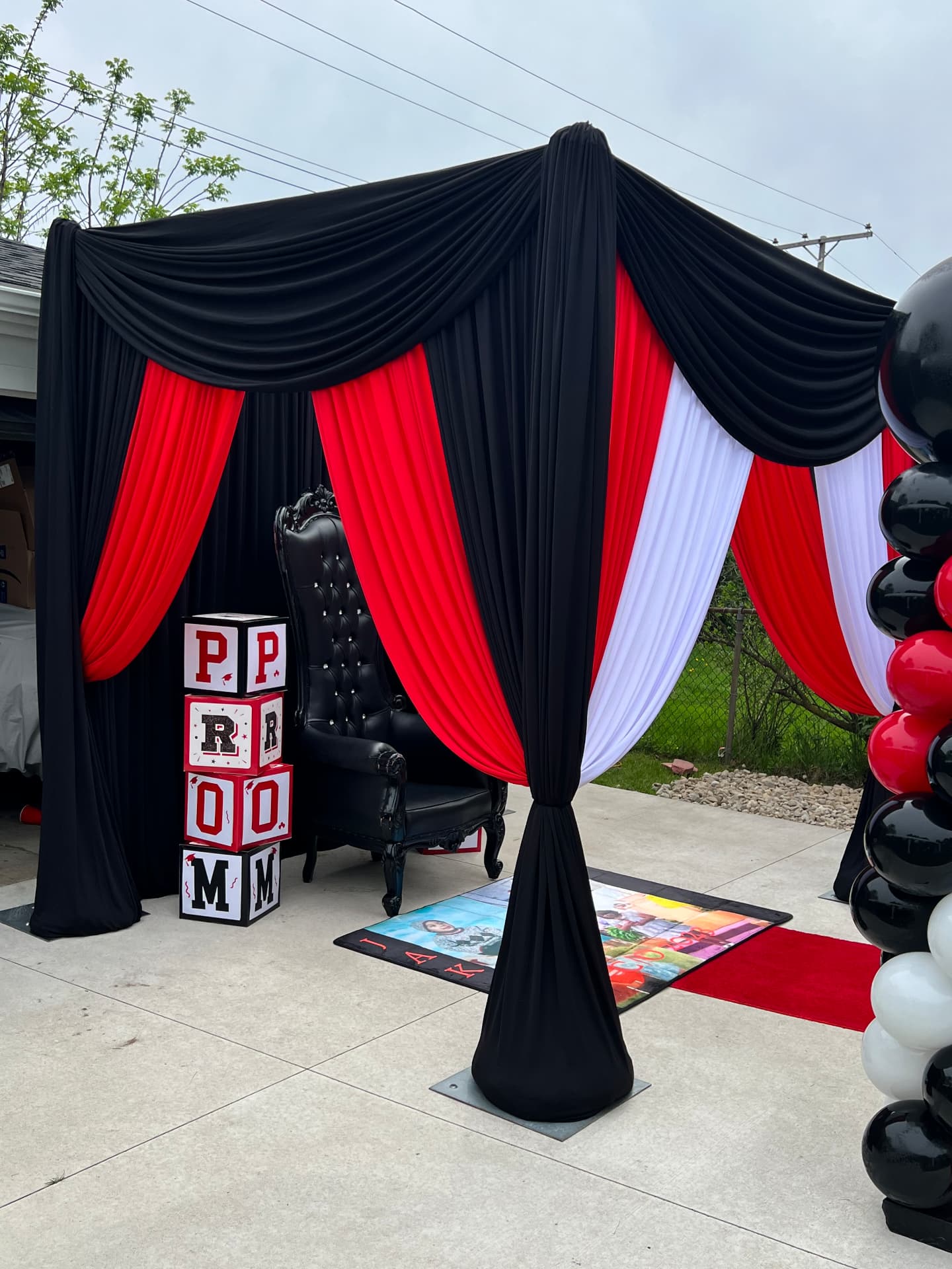 Outdoor prom send-off cabana draped in black, red and white with throne chair